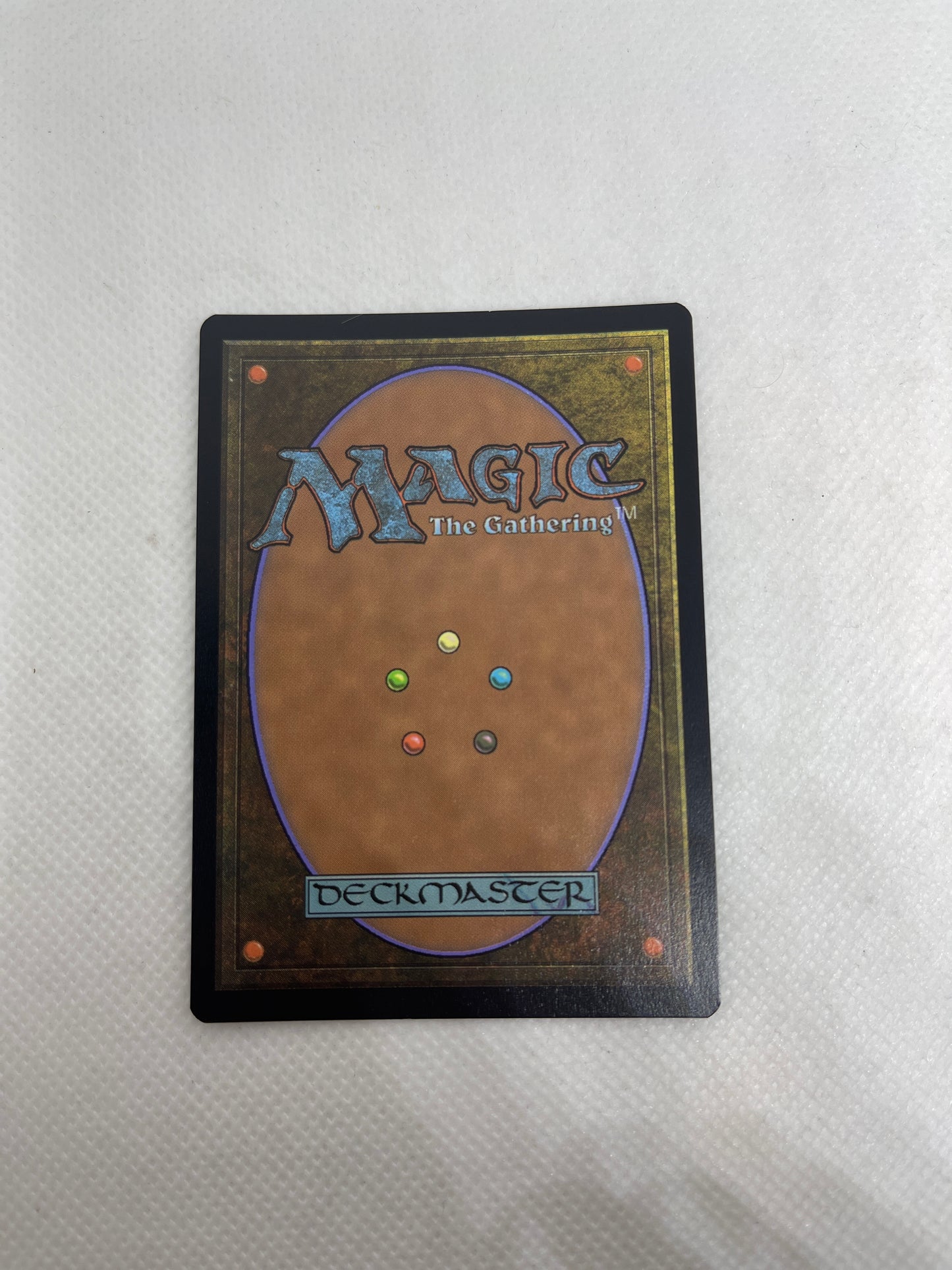 Trading card with 'Magic: The Gathering' logo and multicolored gems on a textured surface